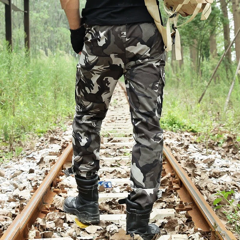 Un hombre que usa pantalones de camuflaje y una mochila camina por las vías del tren