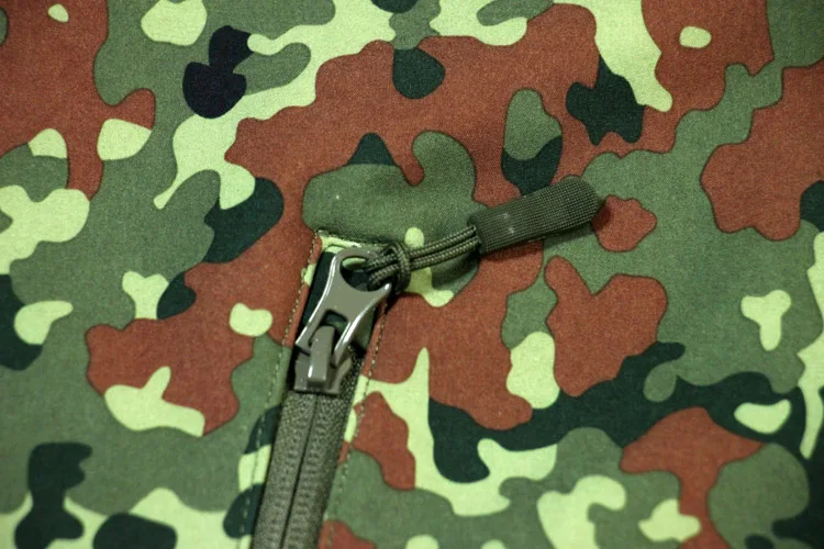 Una tela de camuflaje verde y marrón con cremallera y un anillo de metal