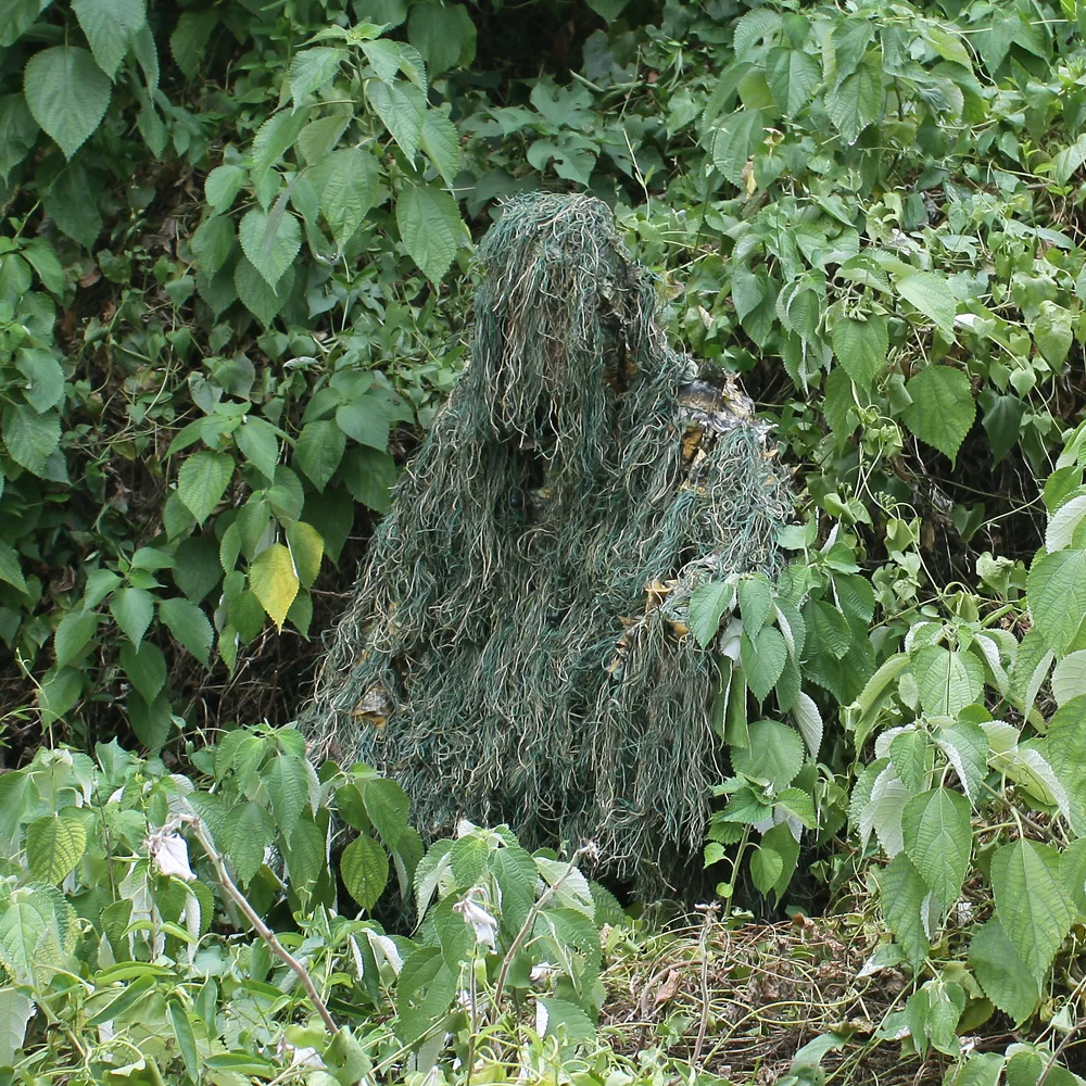 Una persona con un traje de camuflaje verde está sentada en los arbustos
