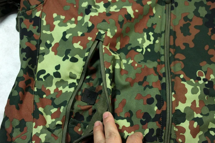 Una mano sostiene una cremallera en la chaqueta de camuflaje