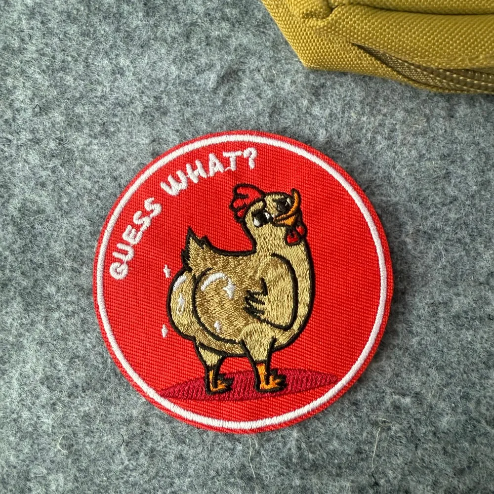 Parche bordado redondo con diseño de pollo y texto «Adivina qué»
