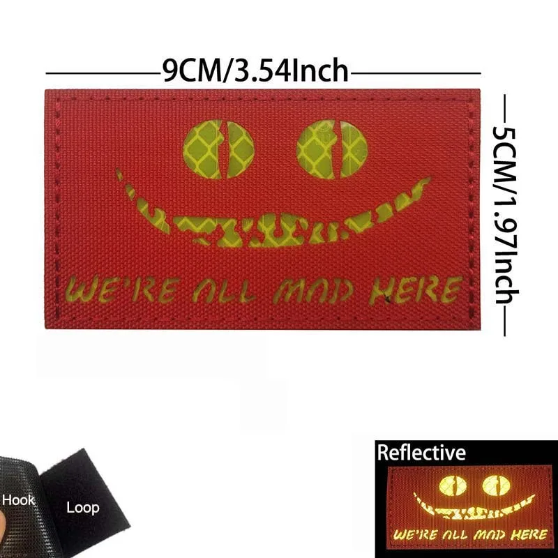 Emblema reflectante WE’RE ALL MAD HERE con motivo de ojo de gato