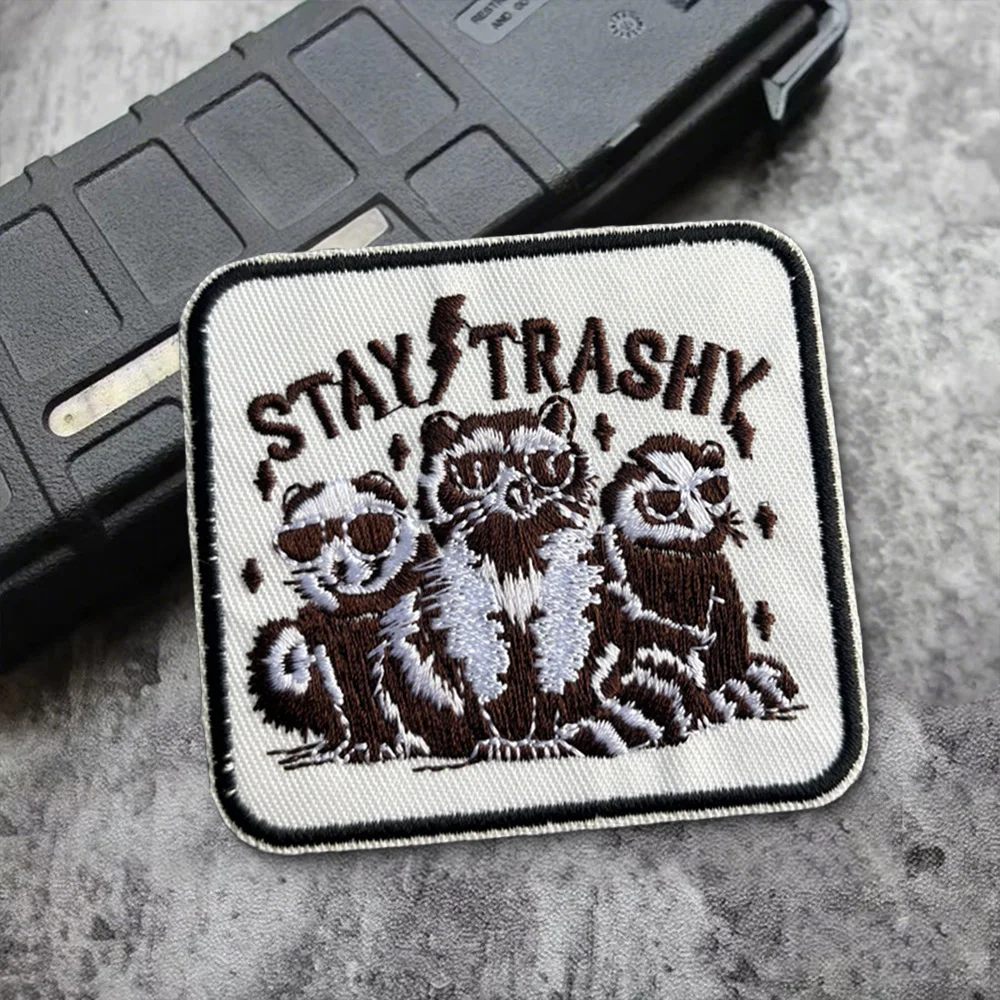 Vista frontal del parche táctico Stay Trashy Morale con diseño de mapache y zarigüeya