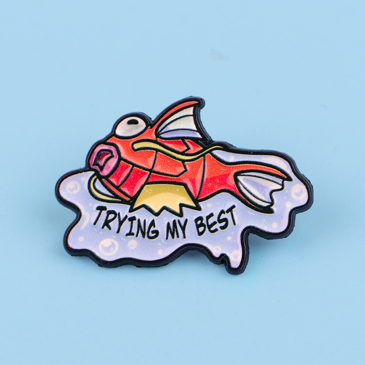 Pin de esmalte con forma de pez y frase “TRYING MY BEST”