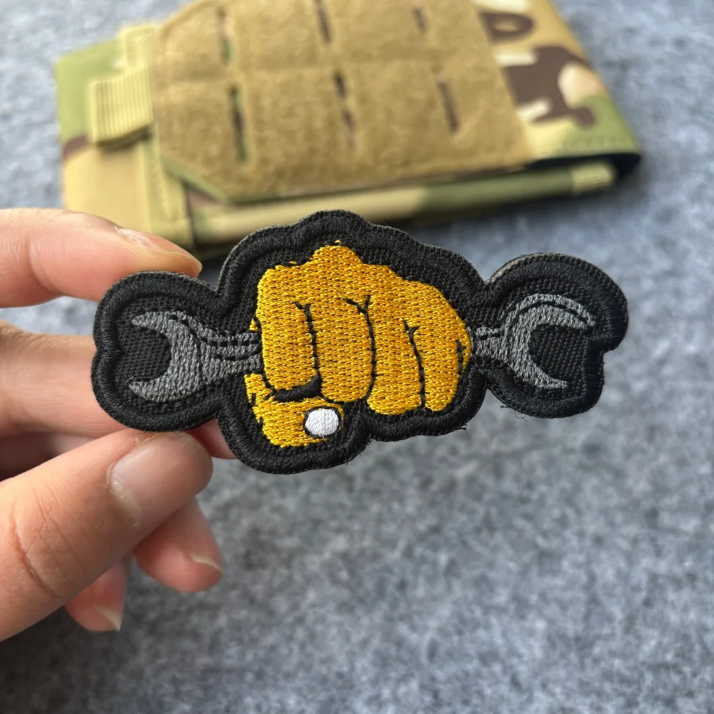 Vista frontal del parche táctico bordado con diseño de puño y llave inglesa sobre fondo negro