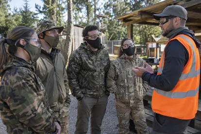 Participantes adultos con protección ocular escuchan la charla de seguridad de un organizador de airsoft