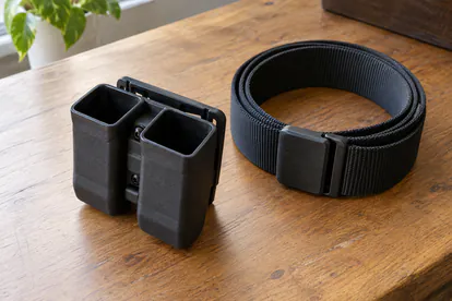 Funda doble vacía para cargadores junto a un cinturón enrollado sobre una mesa